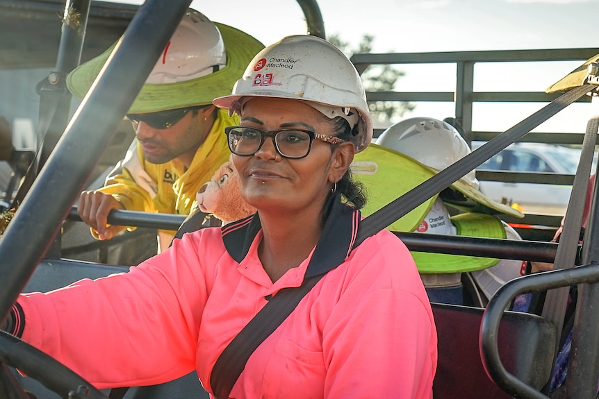 A woman wearing pink work clothes and a safety helmet is sitting in the car.