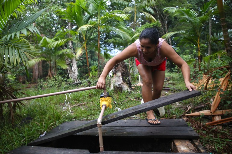 A woman leans over to lift a wooden board from above a well in the Amazon rainforest.