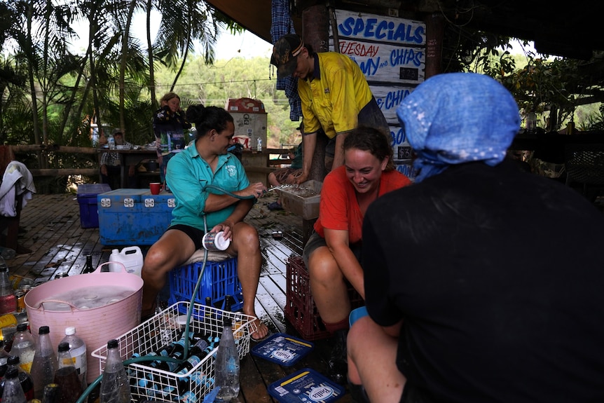 Two women and a man smiled and talked, sorting bottles and other items on a flood-affected deck.