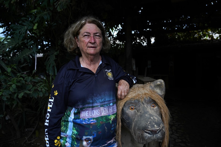 The woman with short curly hair, wearing a long-sleeved dark blue shirt, leaned against the lion statue with a serious expression.