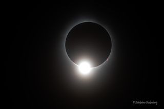 The eclipsed sun appears as a black circle with a hazy white outline and a bright white circular shape on the lower edge, making the scene look like a diamond ring.