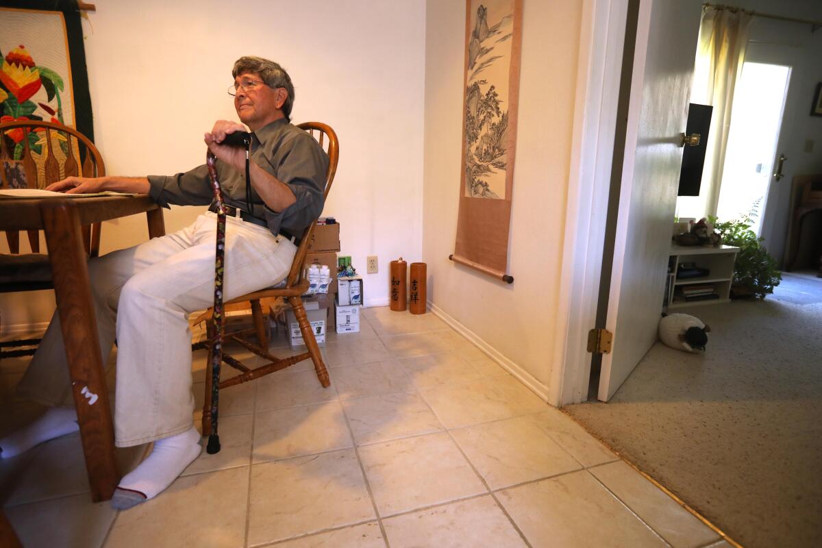 A man sits at a table in his home with a cane.