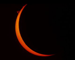 A large portion of the sun is obscured by the moon, leaving a thin orange crescent that looks like a new moon in the night sky.
