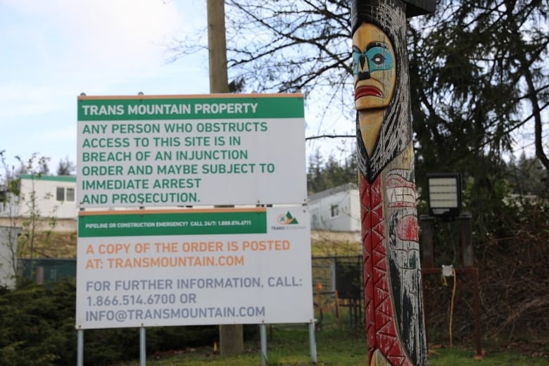 The totem pole sits next to a sign indicating that the property belongs to Trans Mountain.