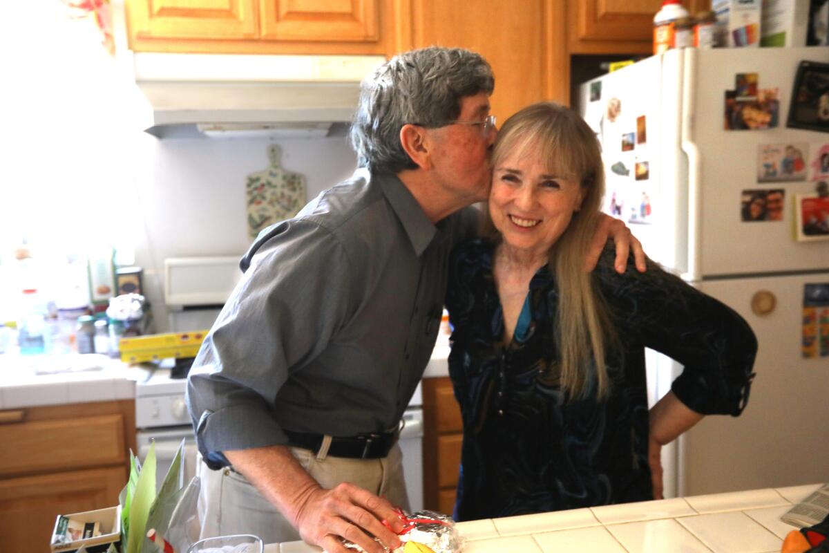 A man kisses his partner in their kitchen. 