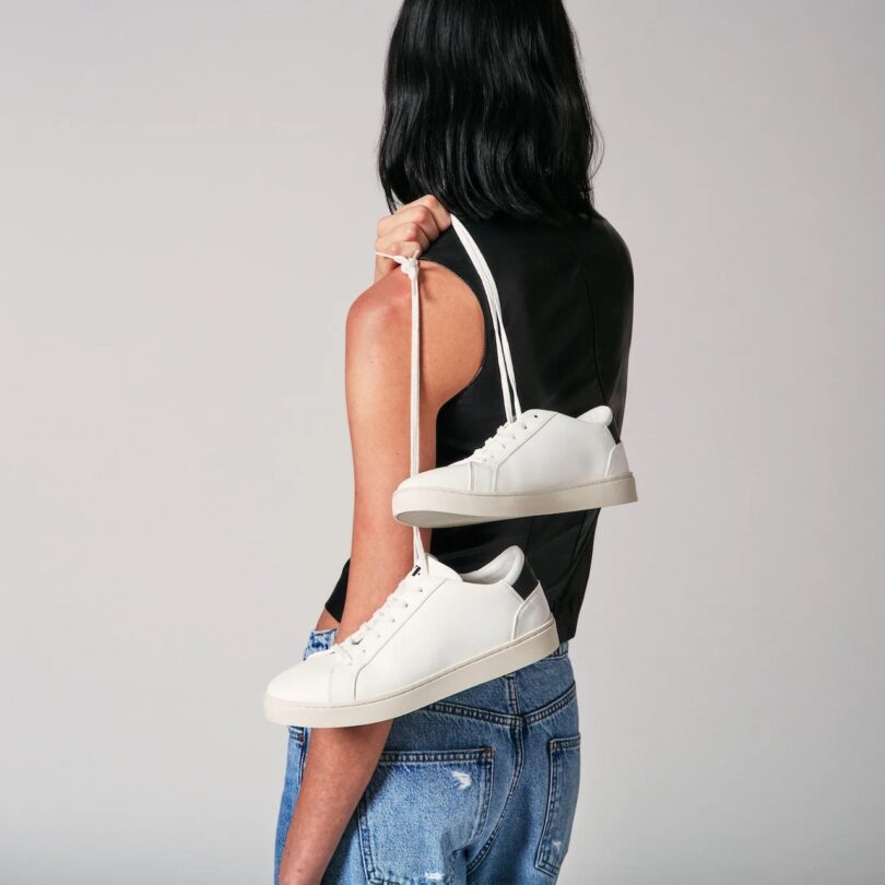 The woman turns around, grabs the laces of her white sneakers and hangs them over her shoulders