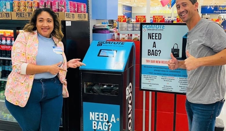 Two Walmart employees stand next to a kiosk where customers can pay to get a reusable bag.