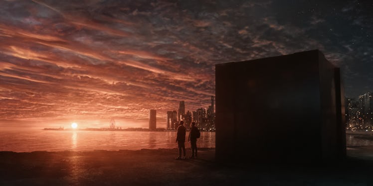 A man and woman stand next to a large cube with the Chicago skyline in the background