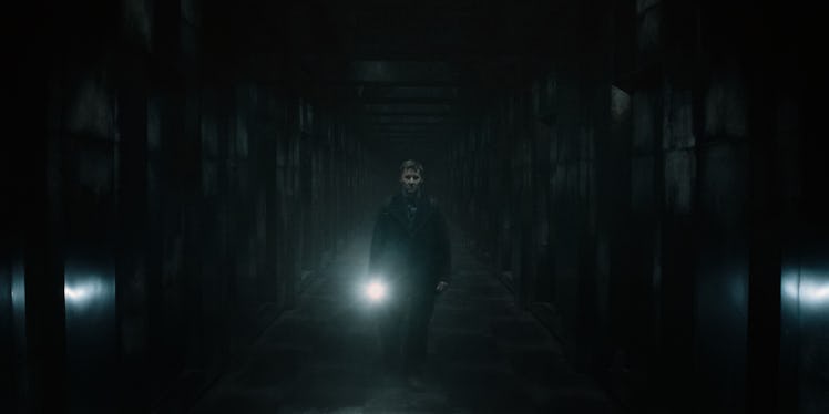 A man holding a lantern walks through a dark corridor lined with doors