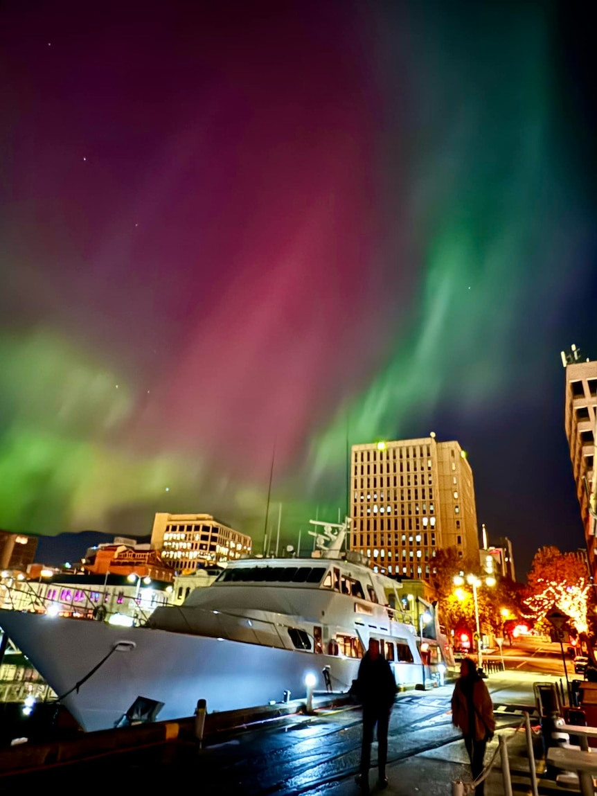The green and pink aurora can be seen behind a large ship moored in the city